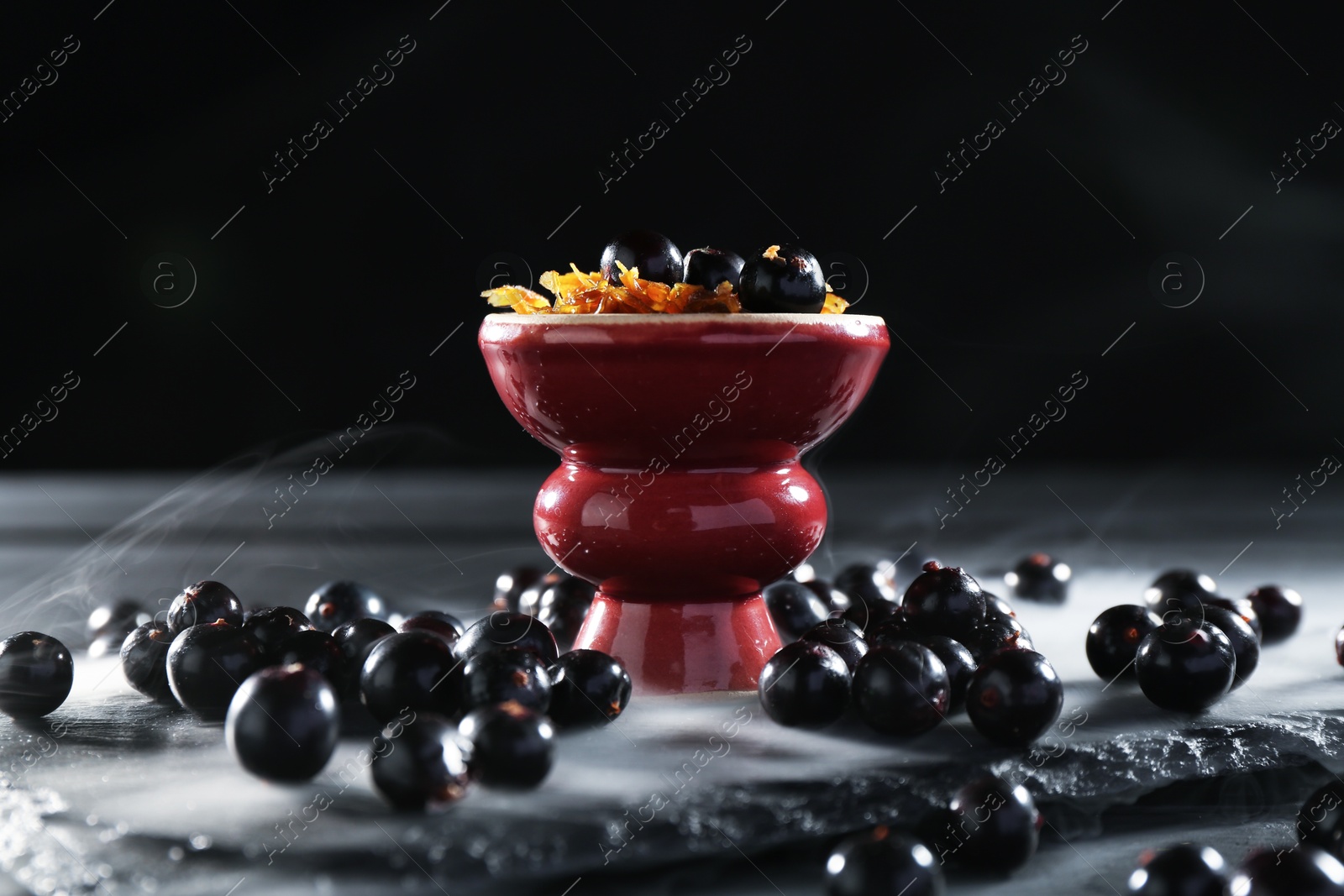Photo of Hookah bowl with currants and smoke on black table, closeup