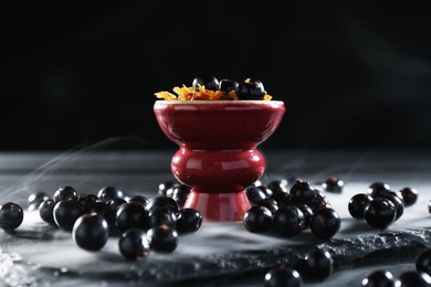 Photo of Hookah bowl with currants and smoke on black table, closeup