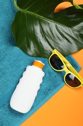 Photo of Beach towel, sunglasses, sunscreen and leaf on orange background, flat lay