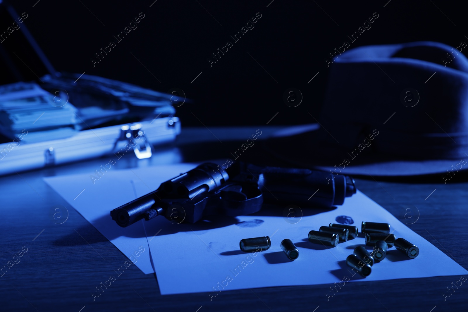Mafia and criminal world. Gun, bullets, fingerprints, briefcase with money and hat on table, toned in blue Photo of Mafia and criminal world. Gun, bullets, fingerprints, briefcase with money and hat on table, toned in blue