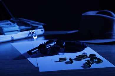 Photo of Mafia and criminal world. Gun, bullets, fingerprints, briefcase with money and hat on table, toned in blue