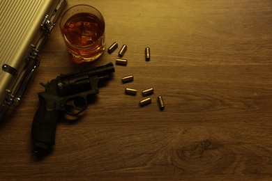 Photo of Mafia and criminal world. Gun, bullets, whiskey and briefcase on wooden table, flat lay. Space for text
