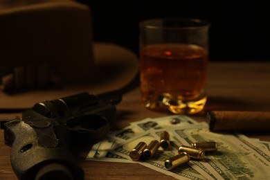 Photo of Mafia and criminal world. Gun, bullets, money, cigar, whiskey and hat on wooden table, closeup
