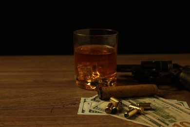 Photo of Mafia and criminal world. Gun, bullets, money, cigar and whiskey on wooden table, closeup