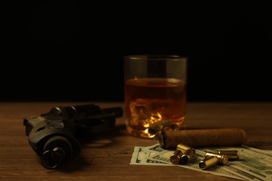 Photo of Mafia and criminal world. Gun, bullets, money, cigar and whiskey on wooden table, closeup
