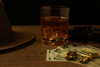 Photo of Mafia and criminal world. Gun, bullets, money, whiskey and hat on wooden table, closeup