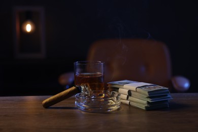 Photo of Ashtray with cigar, money and whiskey on wooden table in mafia boss office