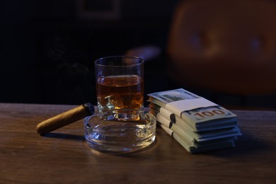 Photo of Ashtray with cigar, money and whiskey on wooden table in mafia boss office