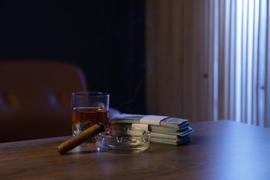 Photo of Ashtray with cigar, money and whiskey on wooden table in mafia boss office. Space for text