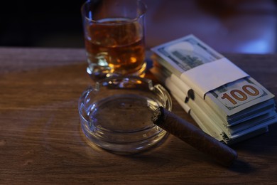 Photo of Mafia and criminal world. Ashtray with cigar, money and whiskey on wooden table, closeup
