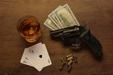 Photo of Mafia and criminal world. Gun, bullets, money, whiskey and playing cards on wooden table, flat lay