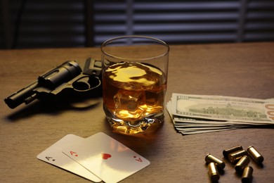 Photo of Mafia and criminal world. Gun, bullets, money, whiskey and playing cards on wooden table, closeup