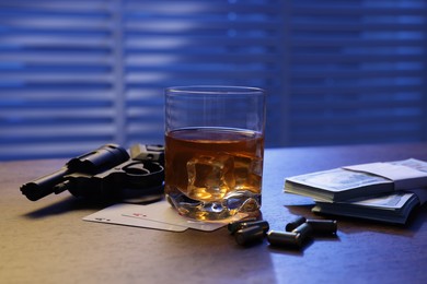 Photo of Mafia and criminal world. Bullets, gun, whiskey, money and playing cards on wooden table indoors, closeup