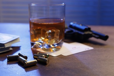 Photo of Mafia and criminal world. Bullets, gun, whiskey, money and playing cards on wooden table indoors, closeup