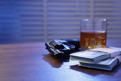 Photo of Mafia and criminal world. Gun, whiskey and money on wooden table indoors, closeup. Space for text