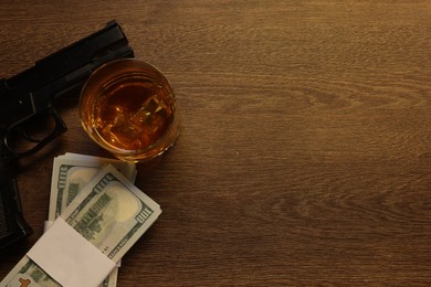 Photo of Mafia and criminal world. Money, whiskey and gun on wooden table, flat lay. Space for text