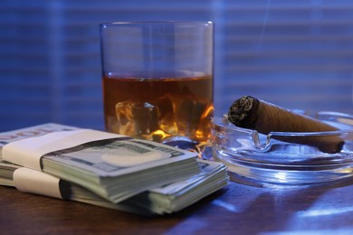 Photo of Mafia and criminal world. Money, ashtray with cigar and whiskey on wooden table, closeup