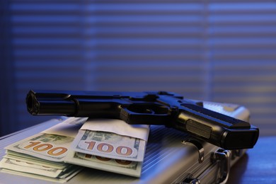 Photo of Mafia and criminal world. Briefcase with money and gun indoors, closeup