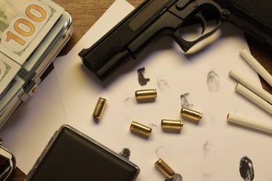 Photo of Mafia and criminal world. Gun, bullets, fingerprints, cigarettes and money on wooden table, flat lay