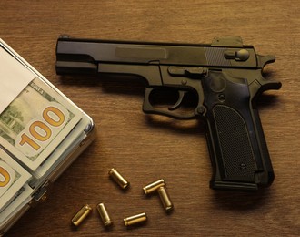Photo of Mafia and criminal world. Gun, bullets and money on wooden table, flat lay