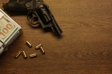 Photo of Mafia and criminal world. Gun, bullets and money on wooden table, flat lay. Space for text