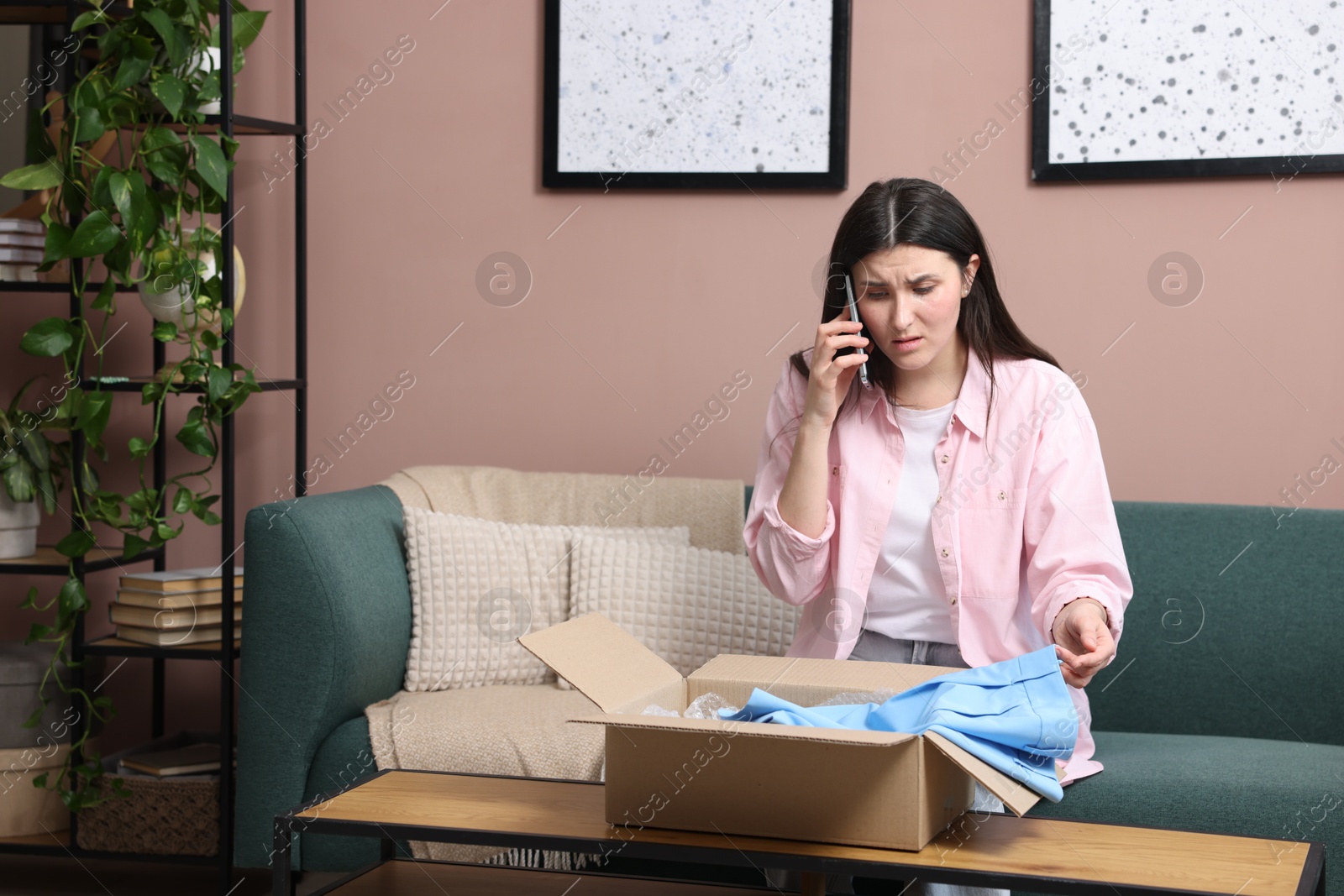 Photo of Young woman with package complaining to customer service via phone at home