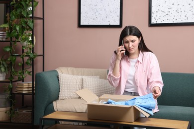 Photo of Young woman with package complaining to customer service via phone at home