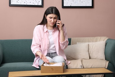 Photo of Young woman with package complaining to customer service via phone at home