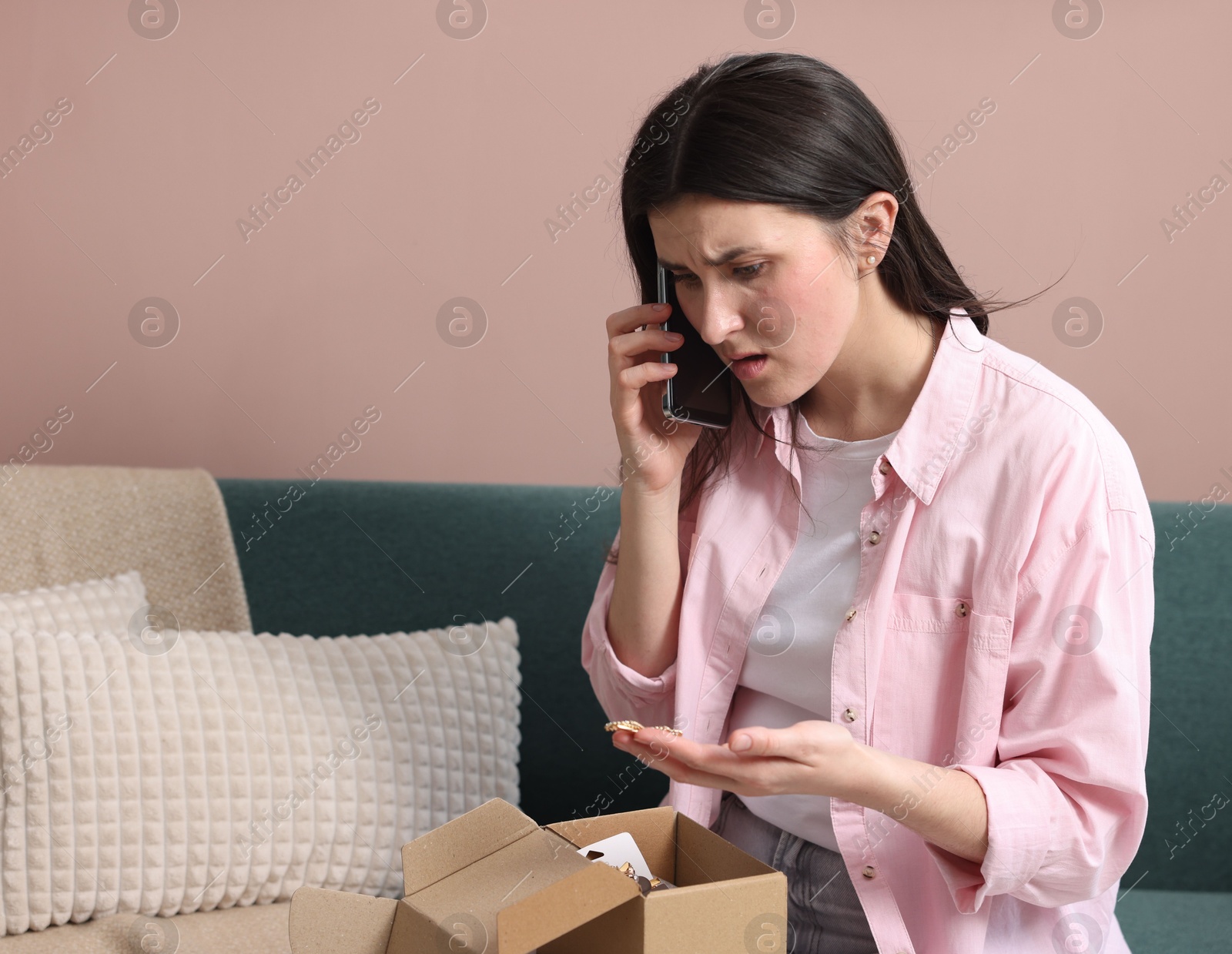 Photo of Young woman with package complaining to customer service via phone at home