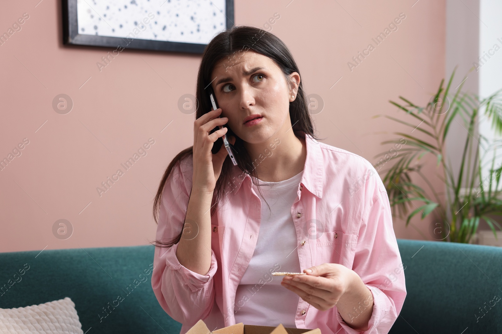 Photo of Young woman with package complaining to customer service via phone at home