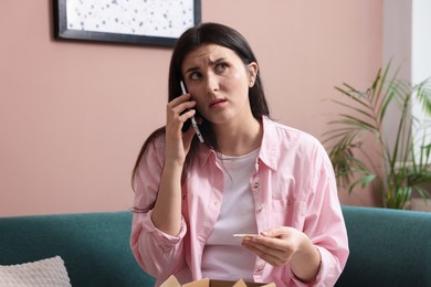 Photo of Young woman with package complaining to customer service via phone at home