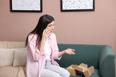 Photo of Young woman with package complaining to customer service via phone at home