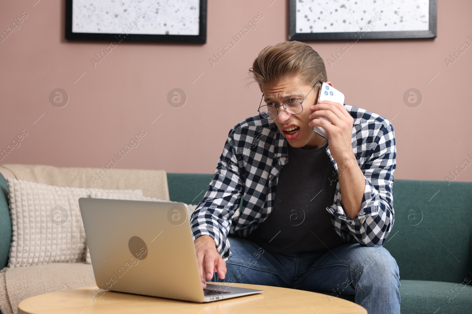 Photo of Young man with laptop complaining to someone via phone at home