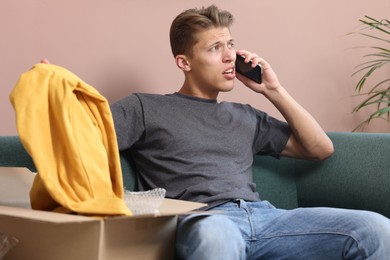Photo of Young man with package complaining to customer service via phone at home