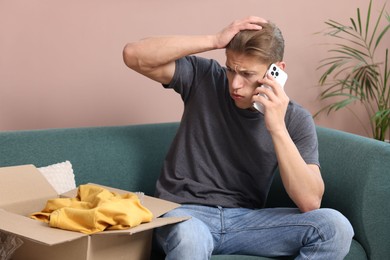 Photo of Young man with package complaining to customer service via phone at home