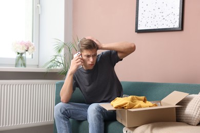 Photo of Young man with package complaining to customer service via phone at home