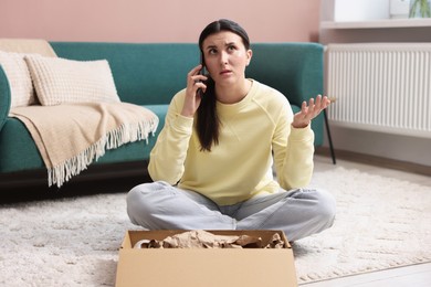 Photo of Young woman with package complaining to customer service via phone at home