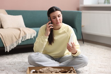 Photo of Young woman with package complaining to customer service via phone at home