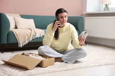 Photo of Young woman with package complaining to customer service via phone at home