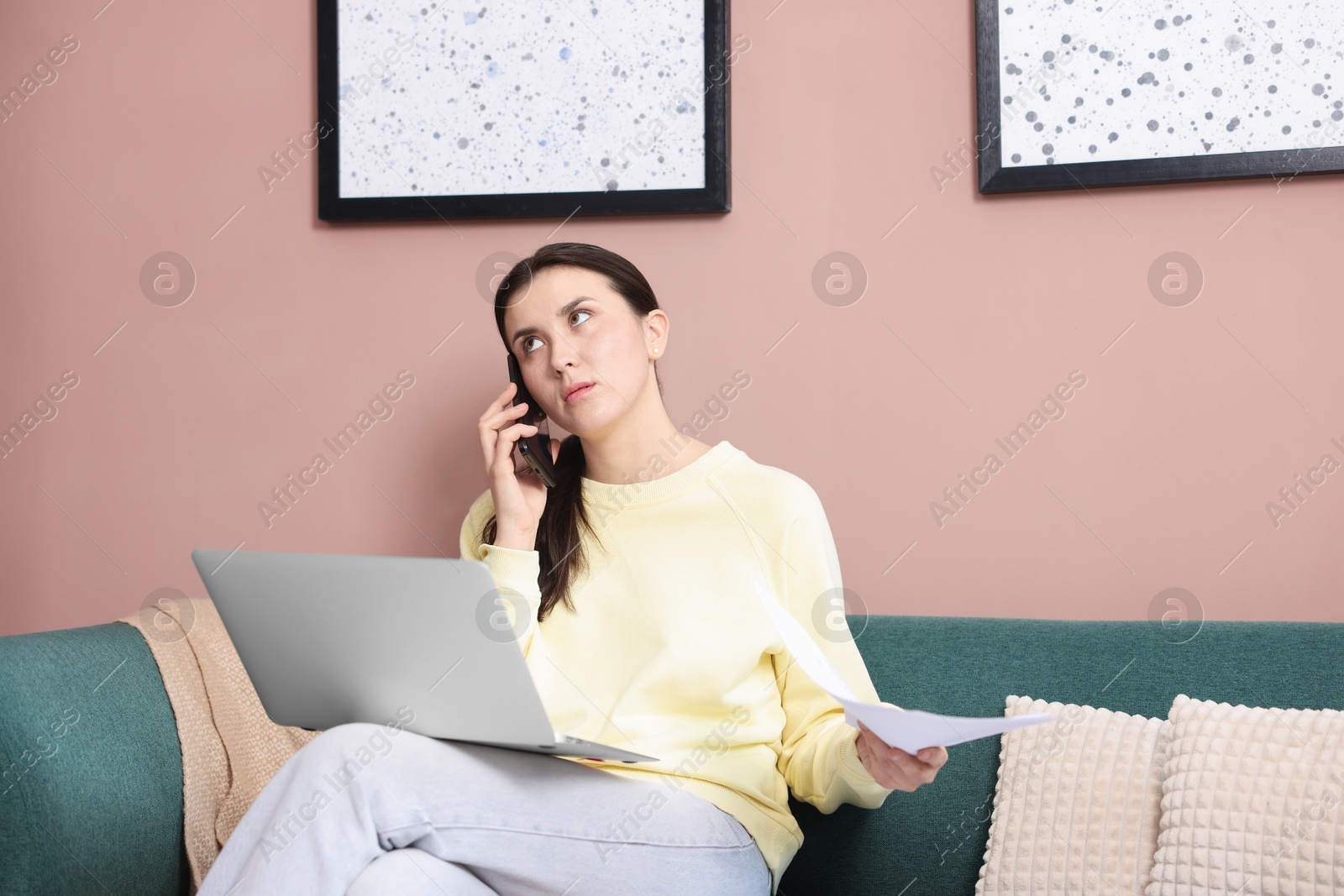 Photo of Young woman with laptop and papers complaining to someone via phone at home