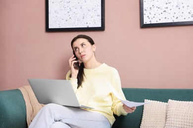 Photo of Young woman with laptop and papers complaining to someone via phone at home