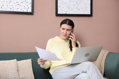 Photo of Young woman with laptop and papers complaining to someone via phone at home