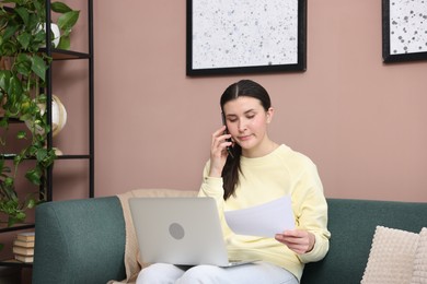 Photo of Young woman with laptop and papers complaining to someone via phone at home