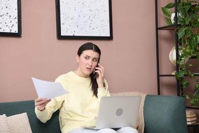 Photo of Young woman with laptop and papers complaining to someone via phone at home