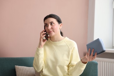 Photo of Young woman with bag complaining to customer service via phone at home