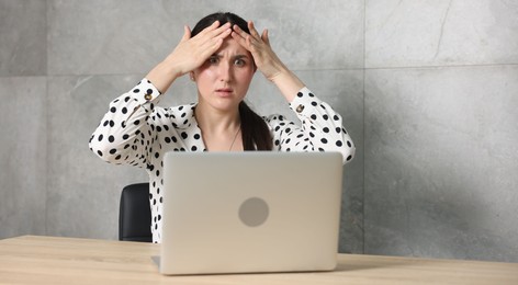 Photo of Young businesswoman with laptop complaining to someone via phone at wooden table indoors