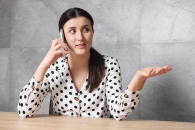 Photo of Young businesswoman complaining to someone via phone at wooden table indoors