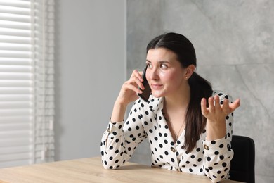 Photo of Young businesswoman complaining to someone via phone at wooden table indoors