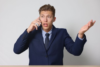 Photo of Young businessman complaining to someone via phone at wooden table indoors
