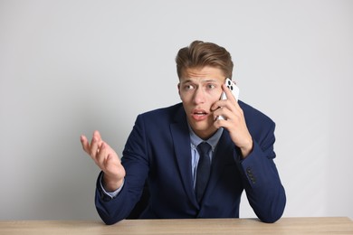 Photo of Young businessman complaining to someone via phone at wooden table indoors